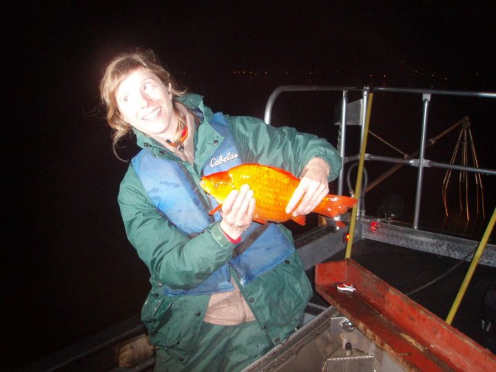 Female scientist in green coat holds large orange goldfish