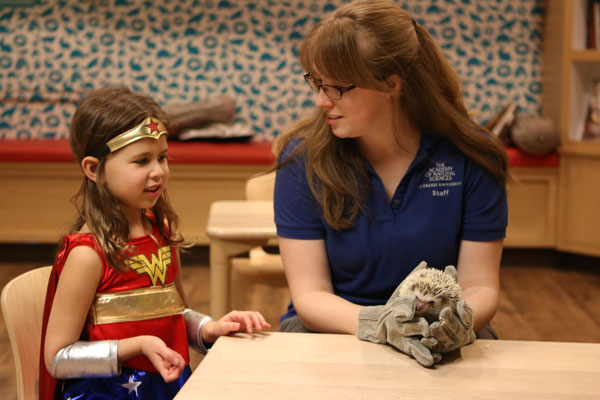 Child dressed as superhero checks out hedgehog. Early registration for summer science camp is open.