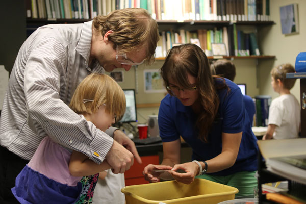 Scientist helps small child with dad do science experiment at Members night. Buy a discounted science museum membership on Cyber Monday.