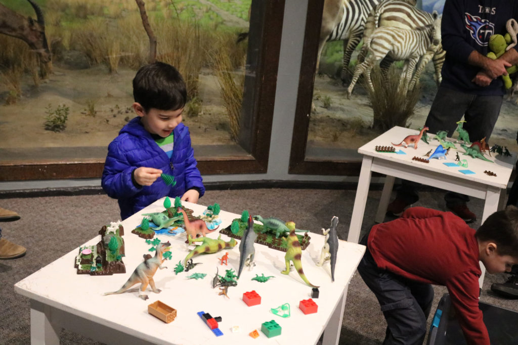 Small boy plays with legos and plastic dinosaurs at small white table