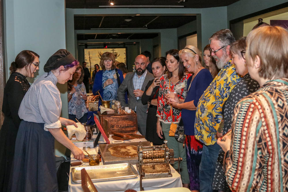 Women dressed in old timely clothing make candy in front of a group