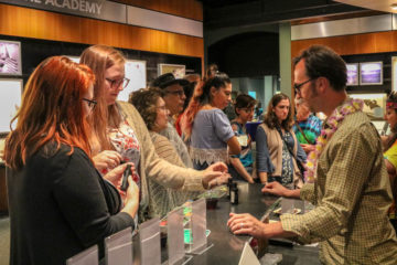 Attendees to Door 19 stand at a counter talking with male educator.