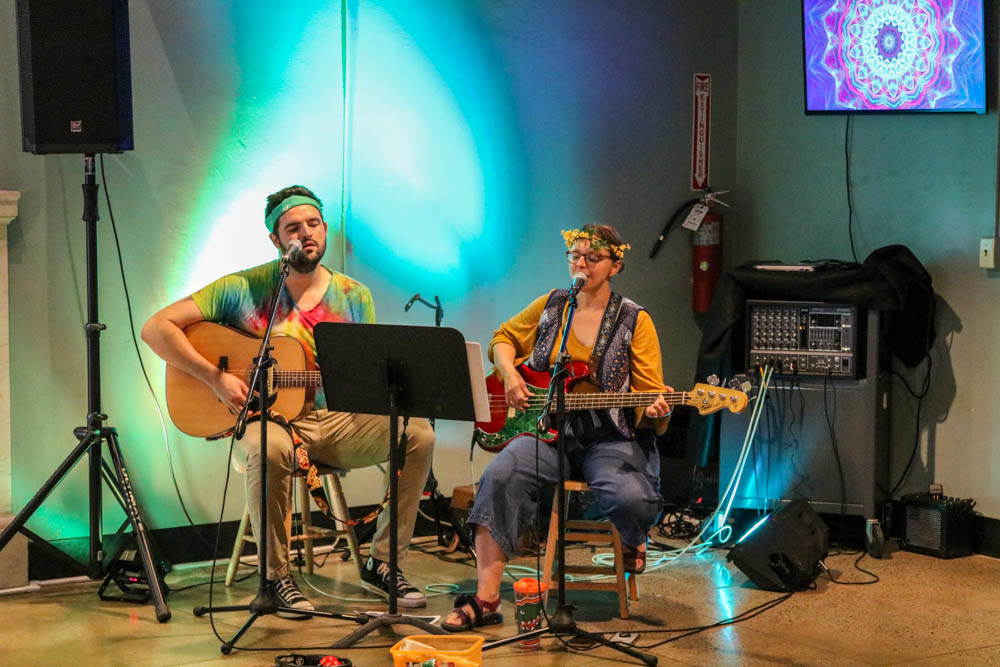 Couple playing guitars and singing, dressed in hippie attire