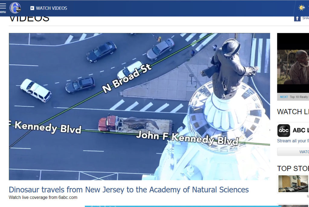 Screenshot from 6ABC live stream of Spinosaurus on flatbed, passing city hall from above