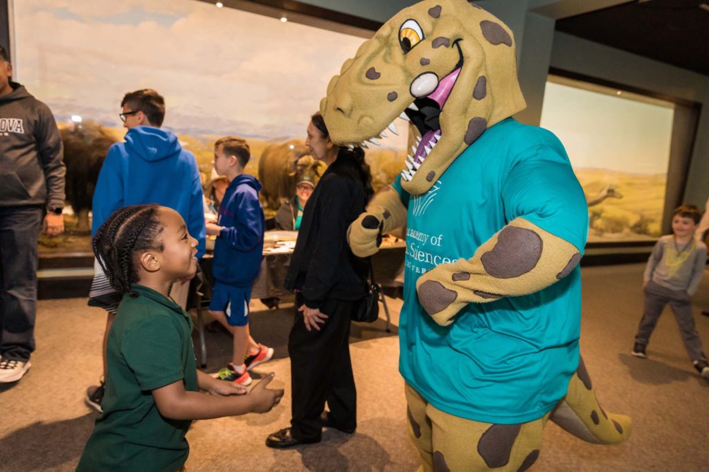 Young boy smiles at Eddie the T. rex, the Academy's mascot