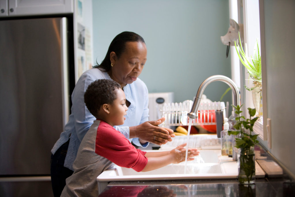 Mom or grandma and young boy wash hands together at sink
