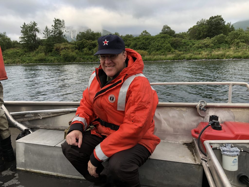 Man in boat with orange safety gear and navy baseball hat