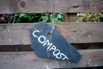 outside of wooden compost bin with black chalk sign with the word compost written on it in white