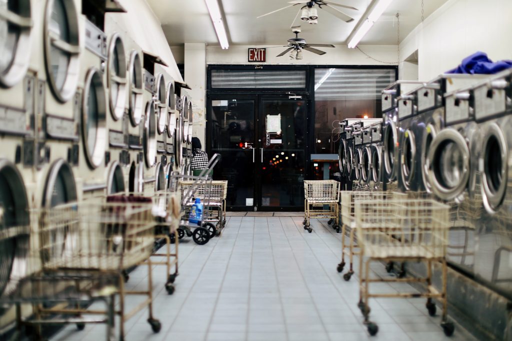 Empty laundromat with white tile floor, open laundry carts and silver machines, looking out toward the exit at nighttime