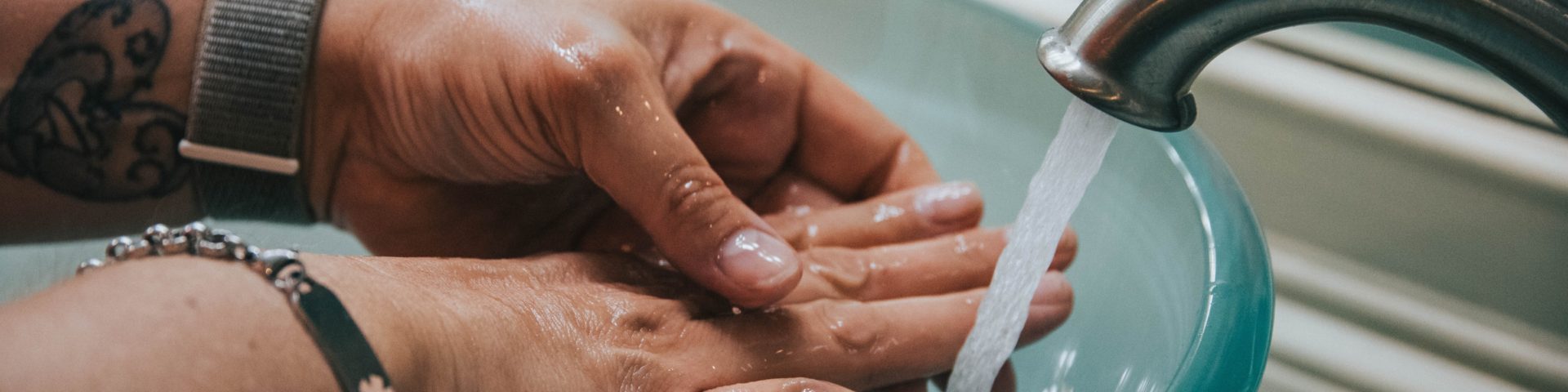 Hands being washed under running water over blue glass sink