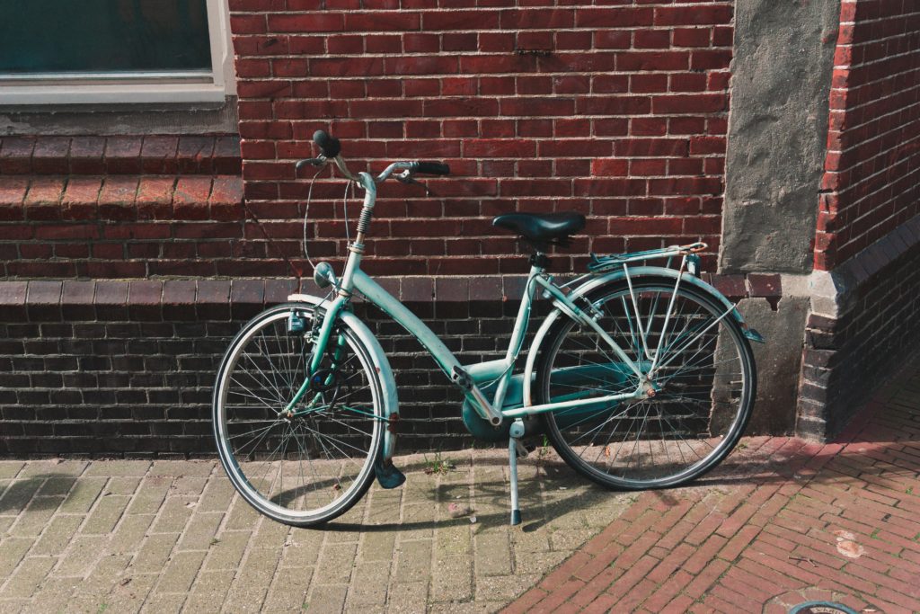 Robin's egg blue old fashioned bicycle with black seat and white kickstand leans against a brick building