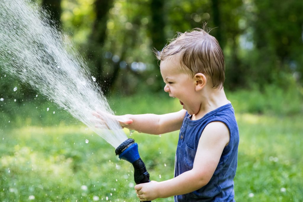 Boy toddler with excited look in navy blue sleeveless shirt with hose shooting water